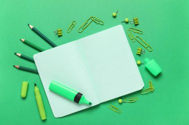 Yeşil arka planda farklı kırtasiye malzemesi olan defteri aç. Okul bitti. Üst görünüm