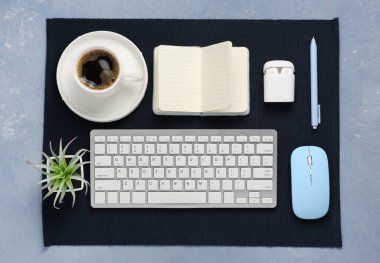 Fare, kulaklık, kahve fincanı ve mavi arka planda not defteri olan modern bilgisayar klavyesi.