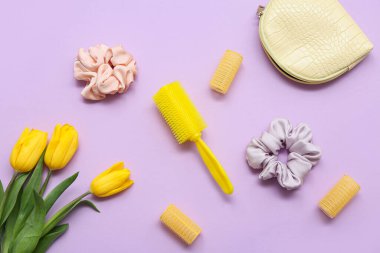 Bigudili makyaj çantası, saç tarağı, ipek tokalar ve mor arka planda lale çiçekleri.