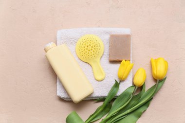 Havlu, saç fırçası, bir şişe şampuan, sabun ve bej arka planda lale çiçeği.
