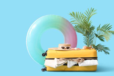 Plaj aksesuarlarıyla dolu bavul, egzotik bitki ve renkli arka planda şişme yüzük.