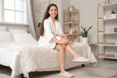 Yatak odasındaki tahta kazıyıcıyla bacağına masaj yapan genç bir kadın.