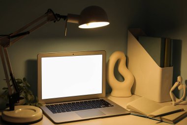 Modern dizüstü bilgisayarı, heykeli ve yeşil duvarın yanında parlayan lambası olan işyeri