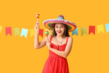 Meksika şapkalı mutlu genç kadın, sarı arka planda marakas ve çelenklerle