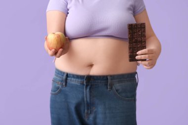 Arkaplanda elma ve çikolata olan kilolu bir kadın. Diyet kavramı
