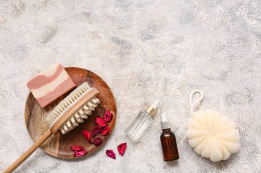 Ahşap tepsi, vücut masajı fırçası, serum şişeleri, gül yaprakları ve grunge arkaplanda sabun kalıbı ile güzel bir kompozisyon.
