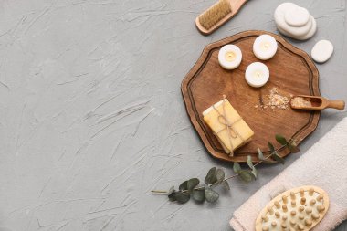 Sabun çubukları, mumlar, okaliptüs dalı ve gri arka planda bir kepçe deniz tuzu olan ahşap tepsi.