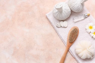 Spa taşları, masaj vücut fırçası, bitkisel torbalar, banyo süngeri, bir şişe serum ve pembemsi çiçekler pembe grunge arka planda.
