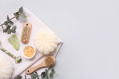 Yüz masajı aletleri, banyo süngeri, havlu, deniz tuzu, vücut masajı fırçası ve beyaz arka planda okaliptüs dalları, yakın plan.