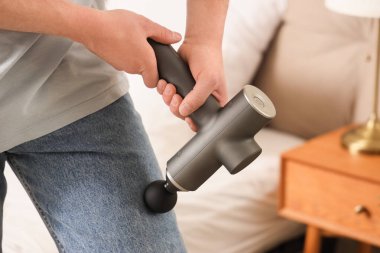 Genç bir adam yatak odasında bacağına perküsyon masajı yapıyor.