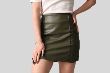 Gri arka planda yeşil deri etek giyen güzel genç bir kadın.