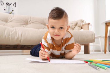 Evinde yerde keçeli kalemlerle çizen sevimli küçük çocuk.