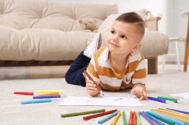 Evinde yerde keçeli kalemlerle çizen sevimli küçük çocuk.