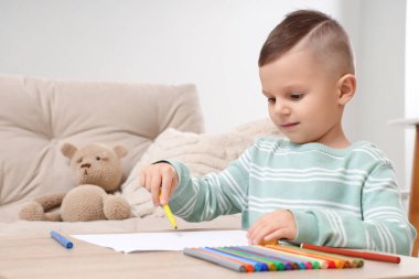 Evdeki masada keçeli kalemle çizen küçük çocuk.