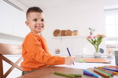 Mutfaktaki masada keçeli kalemlerle resim yapan küçük çocuk.