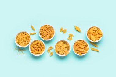 Mavi arka planda farklı lezzetli pişmemiş makarna kaseleri