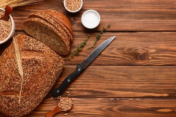 Tahta zemin üzerinde dilimlenmiş somun ekmek, buğday dikenleri, tahıllar ve kekik.
