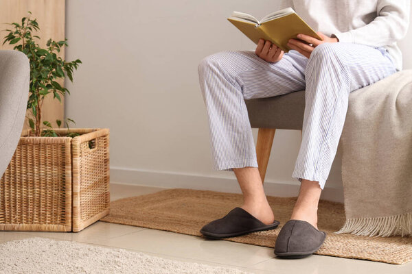 Человек с книгой в тапочках сидит на мягкой скамейке в комнате