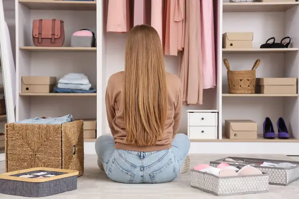 Farklı organizatörlerle temiz giysileri olan güzel genç bir kadın gardıropta oturuyor.