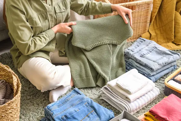 Kadın, yerde otururken temiz giysileri katlıyor.