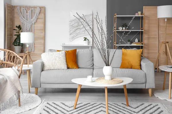 Oturma odasındaki masada söğüt dalları ve fincanı olan bir vazo.