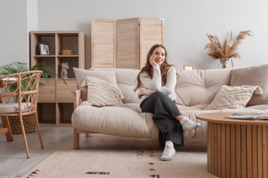 Evdeki yumuşak kanepede oturan genç kadın.