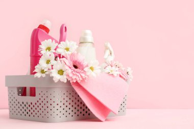 İçinde temizlik malzemeleri, aletler ve pembe arka planda bahar çiçekleri olan sepet.
