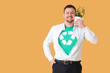 Geri dönüşüm işaretli tişörtlü genç adam ve sarı arka planda ev bitkisi. Ekoloji kavramı