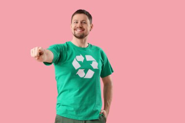 Geri dönüşüm logosu pembe arka plandaki izleyiciyi gösteren tişörtlü mutlu genç adam. Ekoloji kavramı