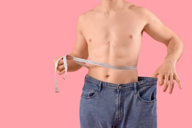 Pembe arka planı olan bol kotlu yakışıklı genç adam, yakın plan. Kilo verme konsepti