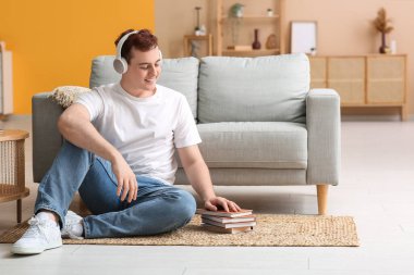 Genç adam sesli kitap dinliyor ve oturma odasında yerde oturuyor.