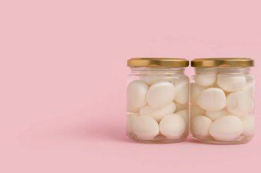 Pembe arka planda haşlanmış bıldırcın yumurtaları olan kavanozlar.