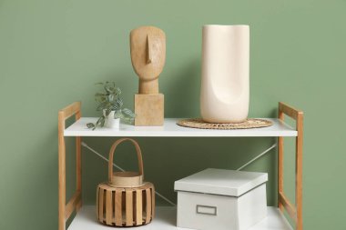 Yeşil duvarın yanında dekoru ve dekoru olan modern raf ünitesi.