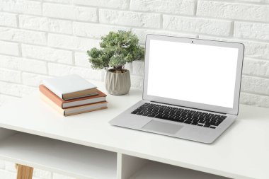 Ofiste beyaz tuğla duvarın yanında modern dizüstü bilgisayarı ve ev bitkisi olan şık bir iş yeri.