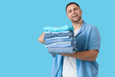 Mavi arka planda bir yığın elbisesi olan genç adam.