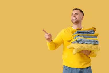 Sarı arka plandaki bir şeyi gösteren bir yığın elbisesi olan genç adam.