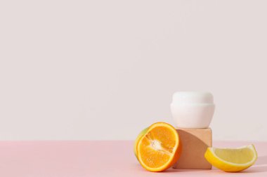 Pembe arka planda turunçgil, alçı tezgahı ve kozmetik ürün parçalarıyla kompozisyon