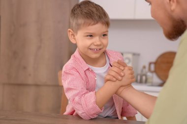 Young man with his little son having arm wrestling in kitchen