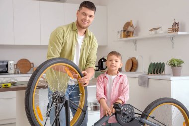 Genç adam ve küçük oğlu evde bisiklet tamir ediyorlar.