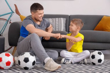 Young man with his little son with football balls bumping fists at home