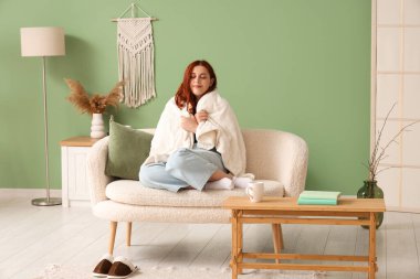 Evdeki kanepede oturan sıcak ekoseli genç kadın.