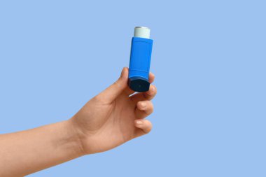 Mavi arka planda modern astım spreyine sahip kadın eli.