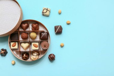 Lezzetli çikolata şekerleriyle dolu bir kutu ve mavi arka planda fındık.