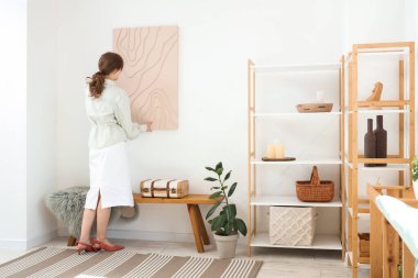 Güzel odadaki beyaz duvara resim asan güzel bir kadın.