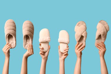 Mavi arka planda farklı terlikler tutan kadın eller.