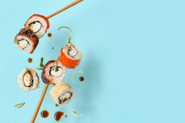 Lezzetli uçan suşi ruloları, soya sosu, salatalık ve yemek çubukları mavi arka planda.