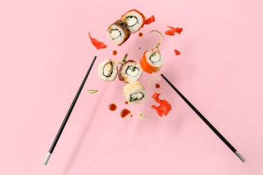 Nefis uçan suşi ruloları, soya sosu, zencefil, salatalık ve pembe arka planda çubuklar.