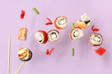 Lezzetli uçan suşi ruloları ve leylak arka planda çubuklar.