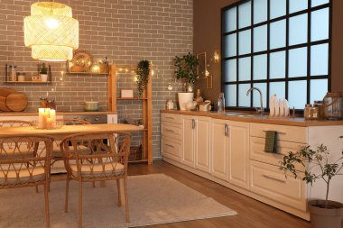 Parlayan lambaları, beyaz tezgahları, çiçekleri, masası ve akşam sandalyeleri olan şık bir mutfak.