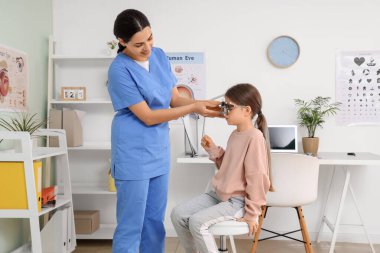 Kadın göz doktoru klinikteki küçük bir kızın deneme çerçevesini çıkarıyor.